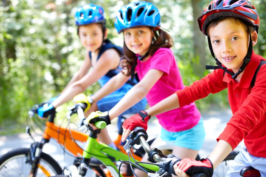 Cette image est l'illustration de trois enfants faisant du vélo, protégés par leur casque et leurs gants